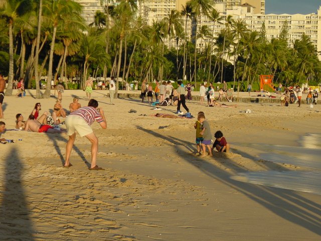 Man bent to take a picture of three children on the beach