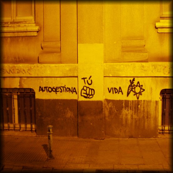 Graffiti on the wall reading "Autogestiona tu vida" and showing a carrot and a sun.