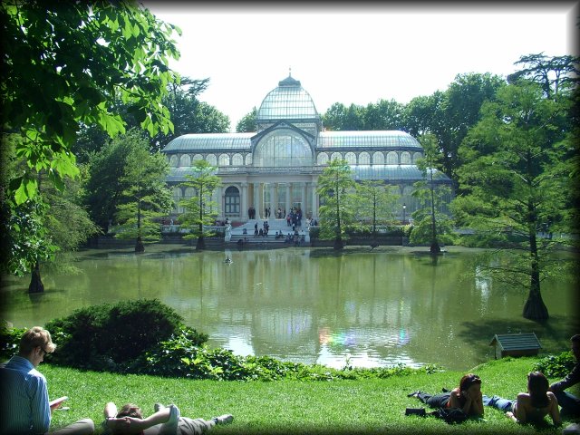 People enjoying the sun in the lawn by the pond in front of the Palacio de Cristal