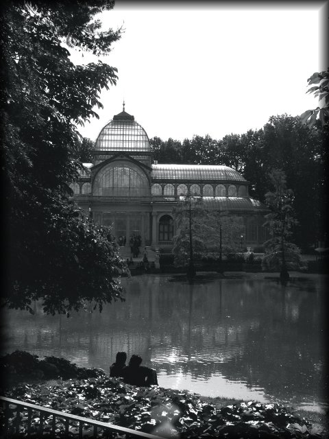 Black and white photo of a couple sitting by the pond in front of the Palacio de Cristal