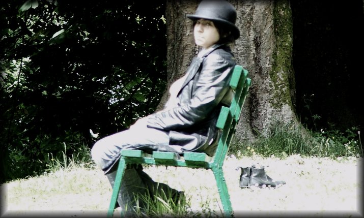 Reuben, the young man in grey and black, sitting on a green bench, under his black bowler hat.