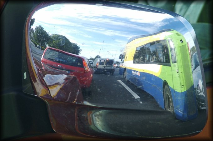 The reflection of cars and the bus we're on, in the chrome rearview mirror of the car next to our bus.