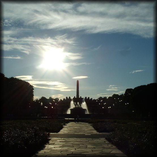 Paved path among flowers, fountain and Monolith (over 14 meter tall column with human bodies carved out of a single block of stone) in the Vigeland Sculpture Park.