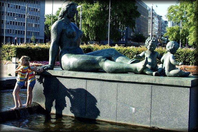 Two twin little sisters in shorts and barefeet in a fountain.