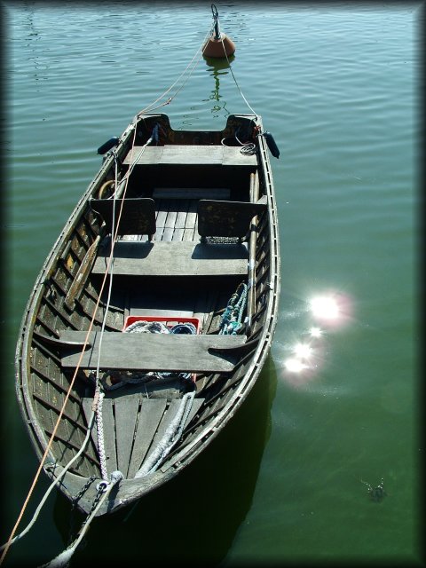 The sun reflected in the green water next to a rowing boat.